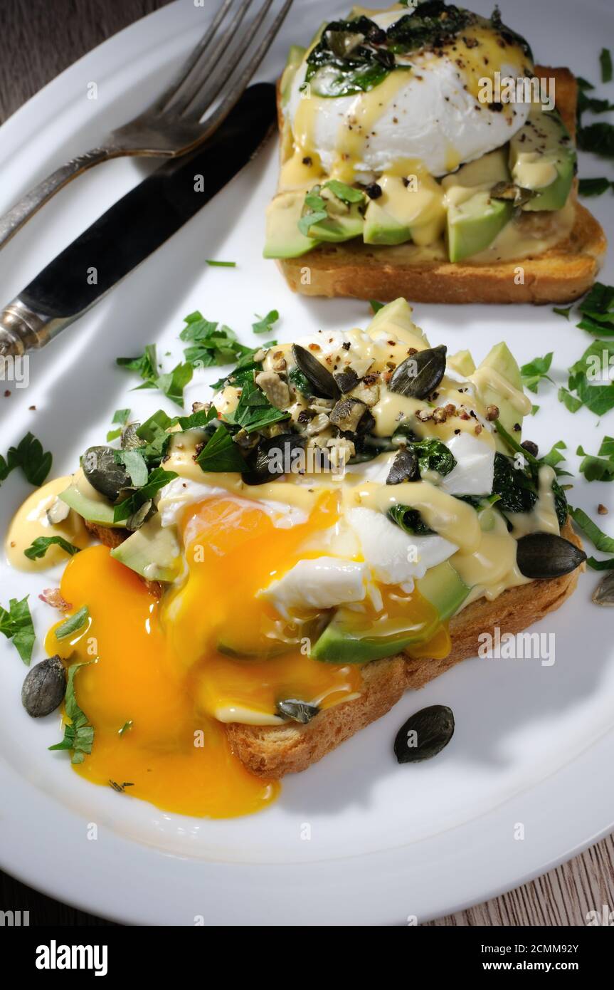 Eggs Benedict on toast with Dutch sauce, slices of avocado Stock Photo