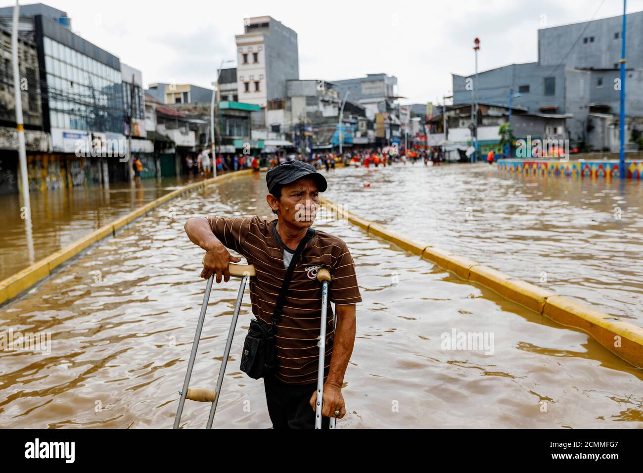 A man uses crutches to walk through floodwaters at the Jatinegara area