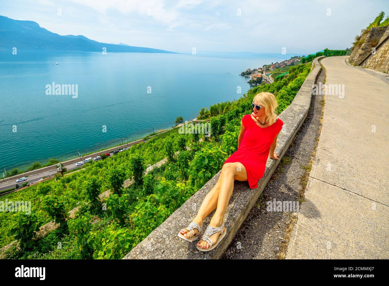 Hiking trail between vineyard terraces overlooking Lake Geneva. Blonde tourist woman enjoying on tour wine tasting in Lavaux Vineyard Terraces Stock Photo