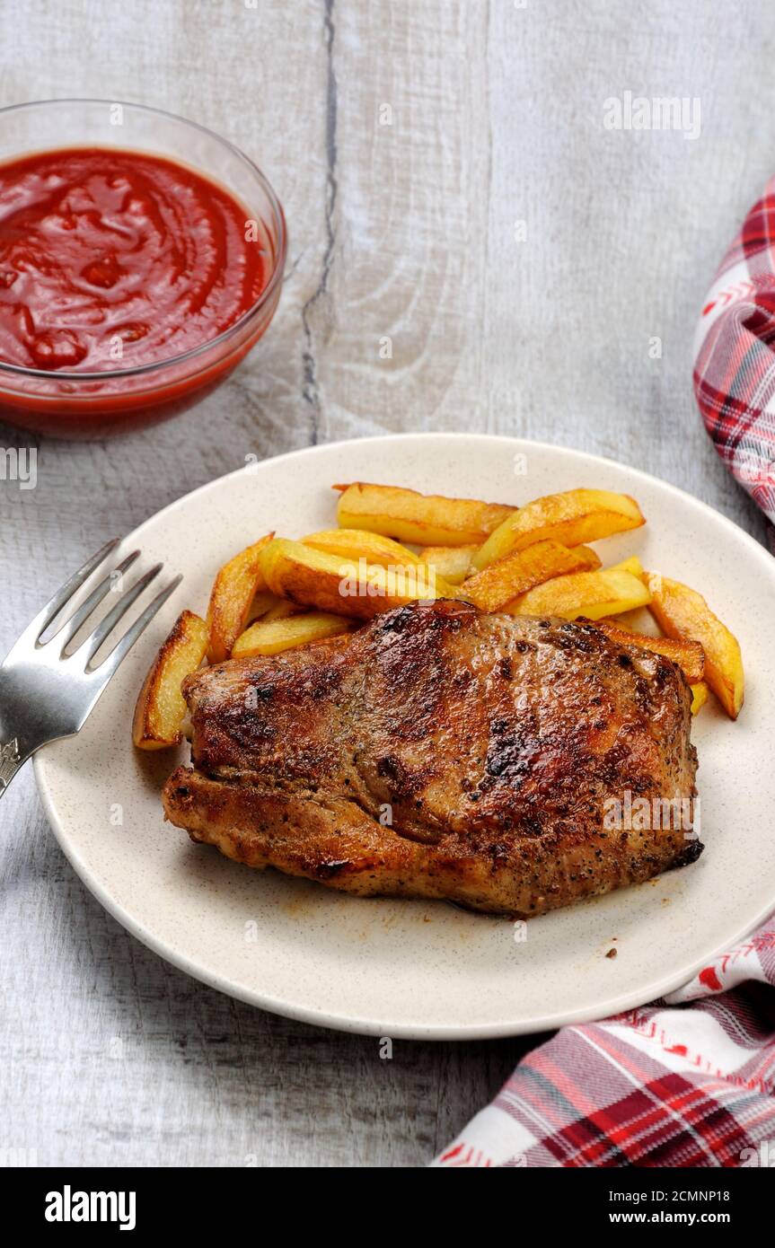 browned pork steak on a bone with fried potatoes. Stock Photo
