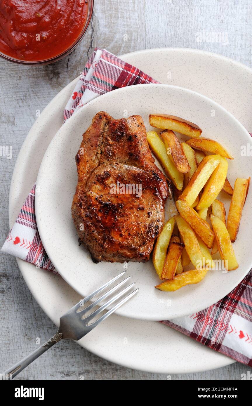 browned pork steak on a bone with fried potatoes. Stock Photo