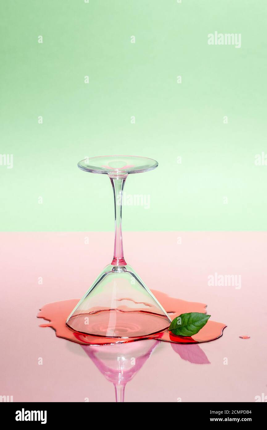 Glass martini glass and spilled liquid on a pink-green background. Modern art photography. Stock Photo
