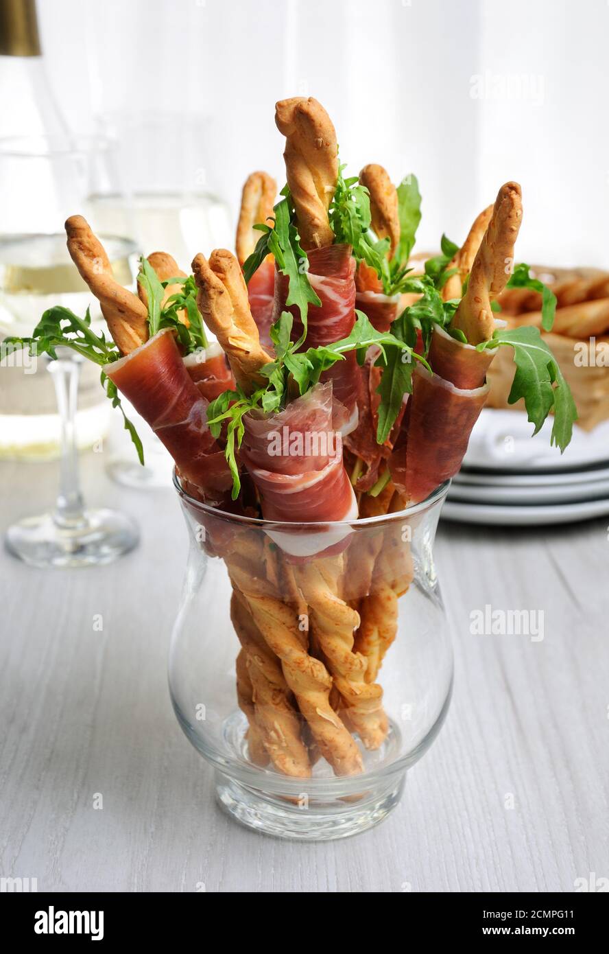 Grissini - bread sticks with Parmesan, wrapped with a piece of prosciutto and arugula. Italian dish Stock Photo
