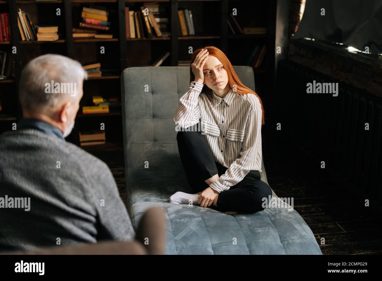 Sad redhead young woman listening to older psychologist doctor explaining treatment. Stock Photo