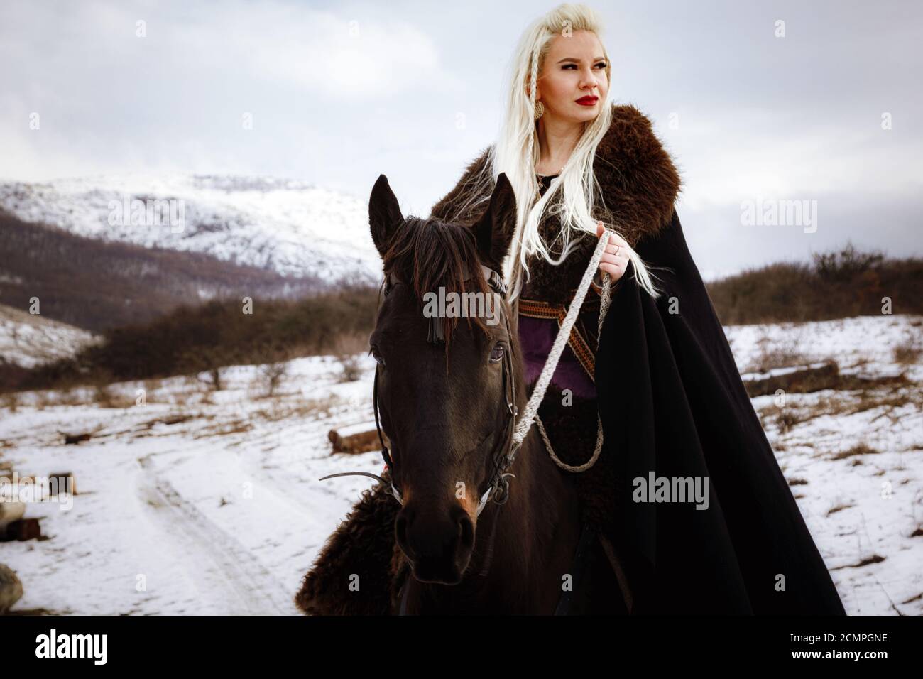 Beautiful young blonde on a crow. Woman viking with a black horse against  the background of mountains. Noble Maidens Stock Photo - Alamy
