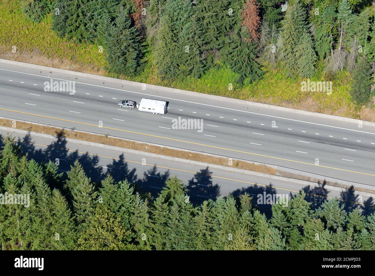 Aerial view of motorhome on highway with vegatation of pine trees around. Single recreational vehicle travelling in empty road. Stock Photo