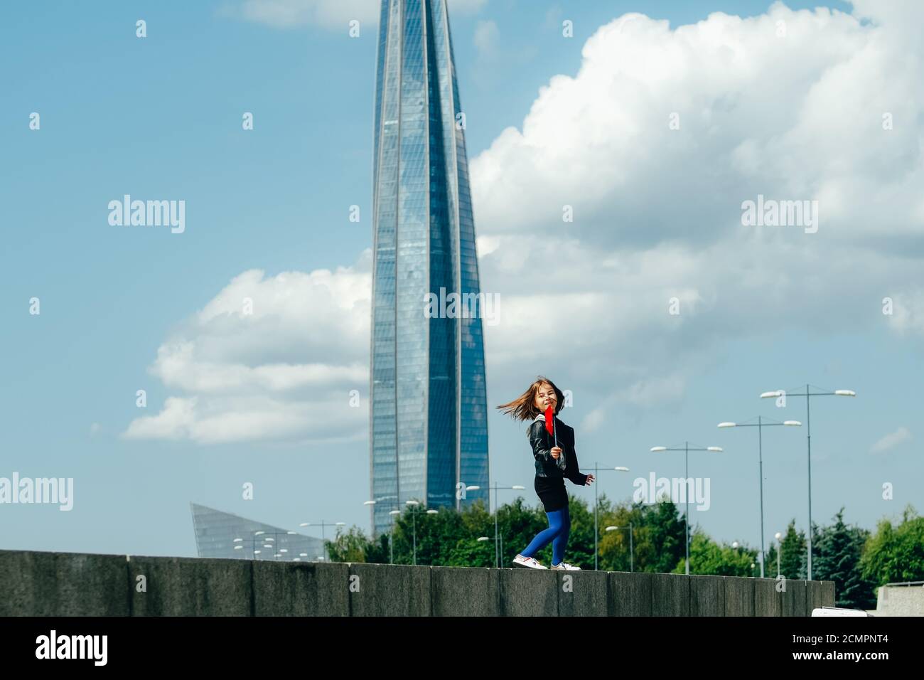 Happy girl with red wind spinner walking on the embankment on blue sky urban background. Freedom concept Stock Photo