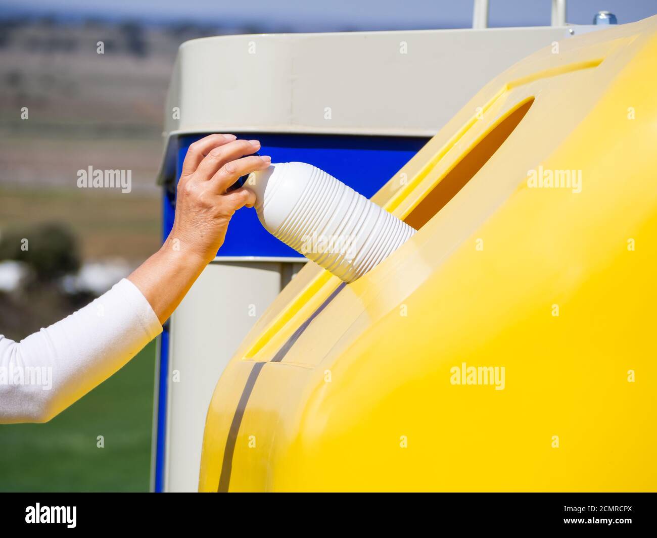 A mature woman pulling a plastic bottle in a yellow bin for recycling plastic Stock Photo