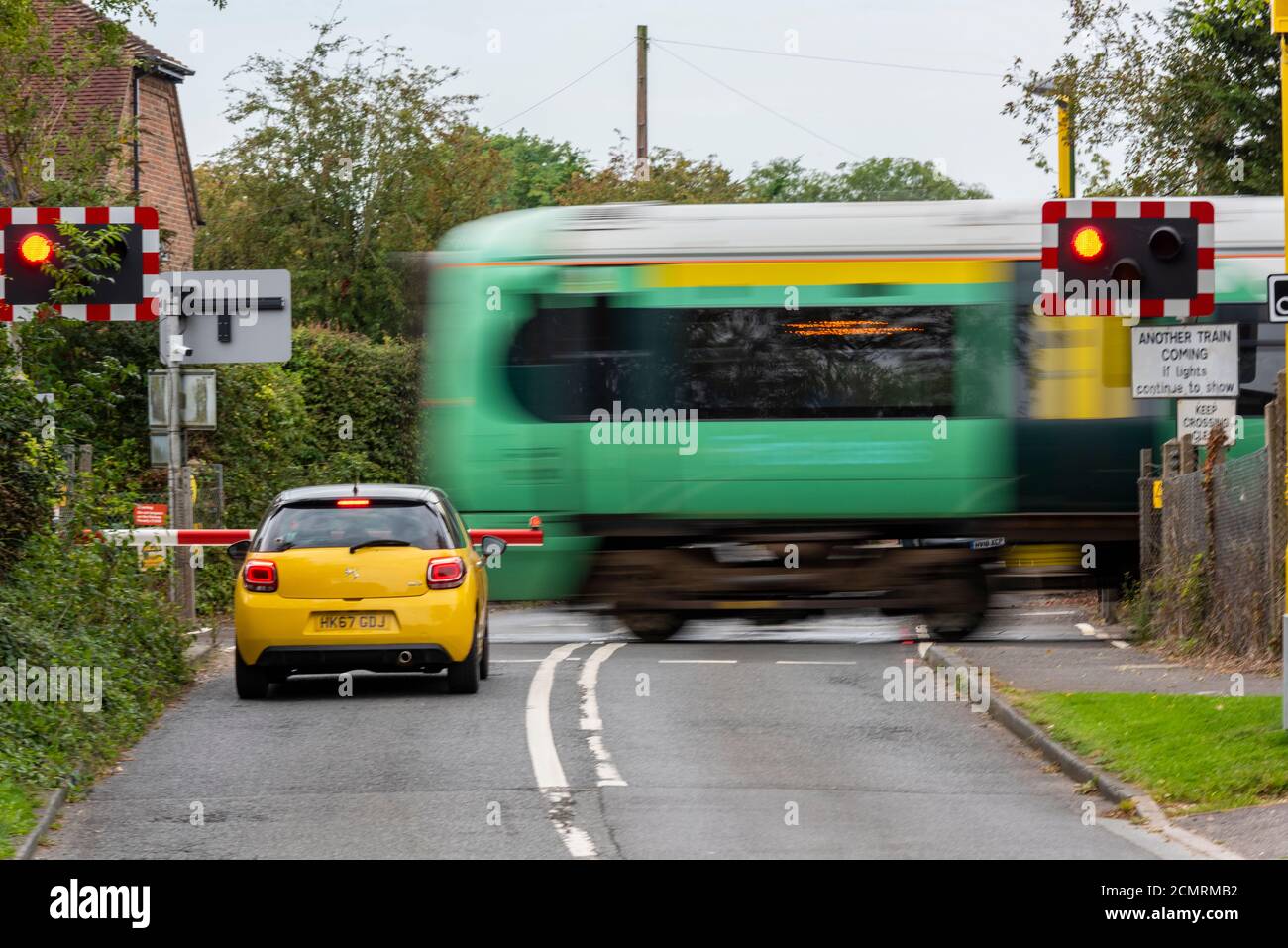 a car waiting at an automatic half barrier level crossing in west sussex while a southern railways train passes over the road. Stock Photo