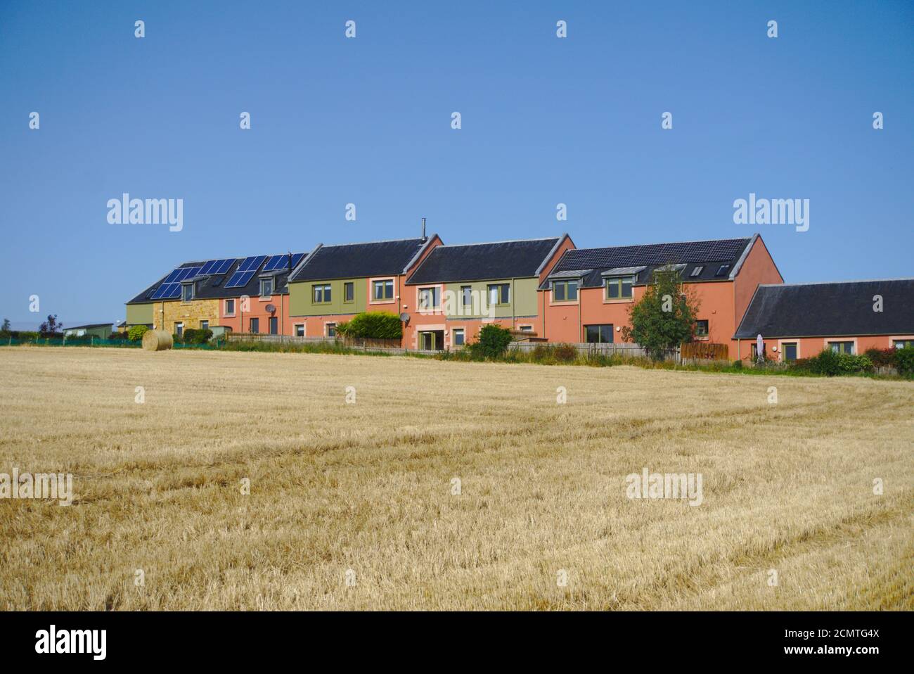 Multi coloured houses, some with solar panels, seen across field in Bolton Steading, Bolton, East Lothian, Scotland, UK. Stock Photo