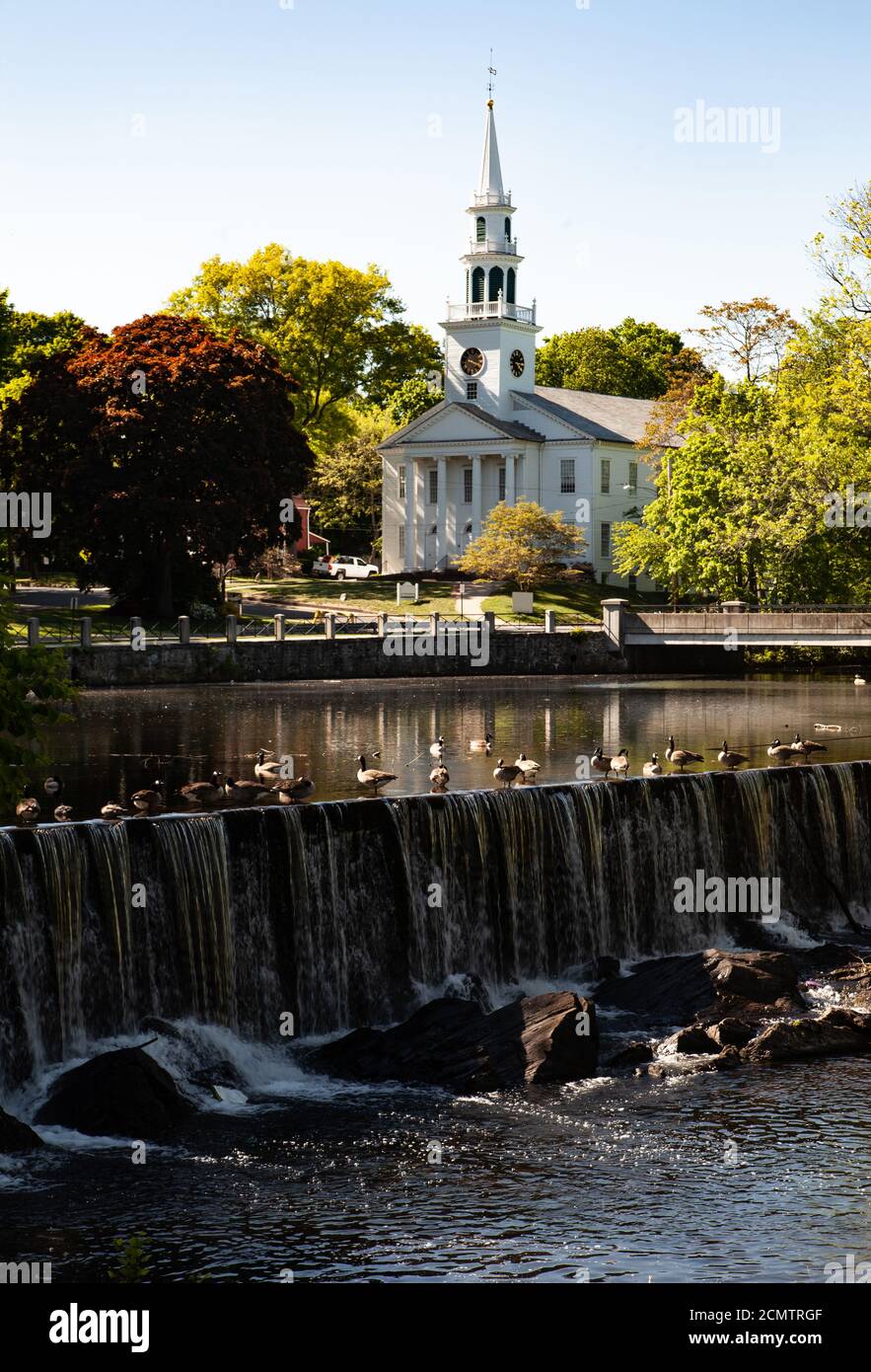 Artificial waterfall with ducks, and white building of church has a roof with a steeple - tower, belfry, lantern, spire among green trees on sunny day Stock Photo