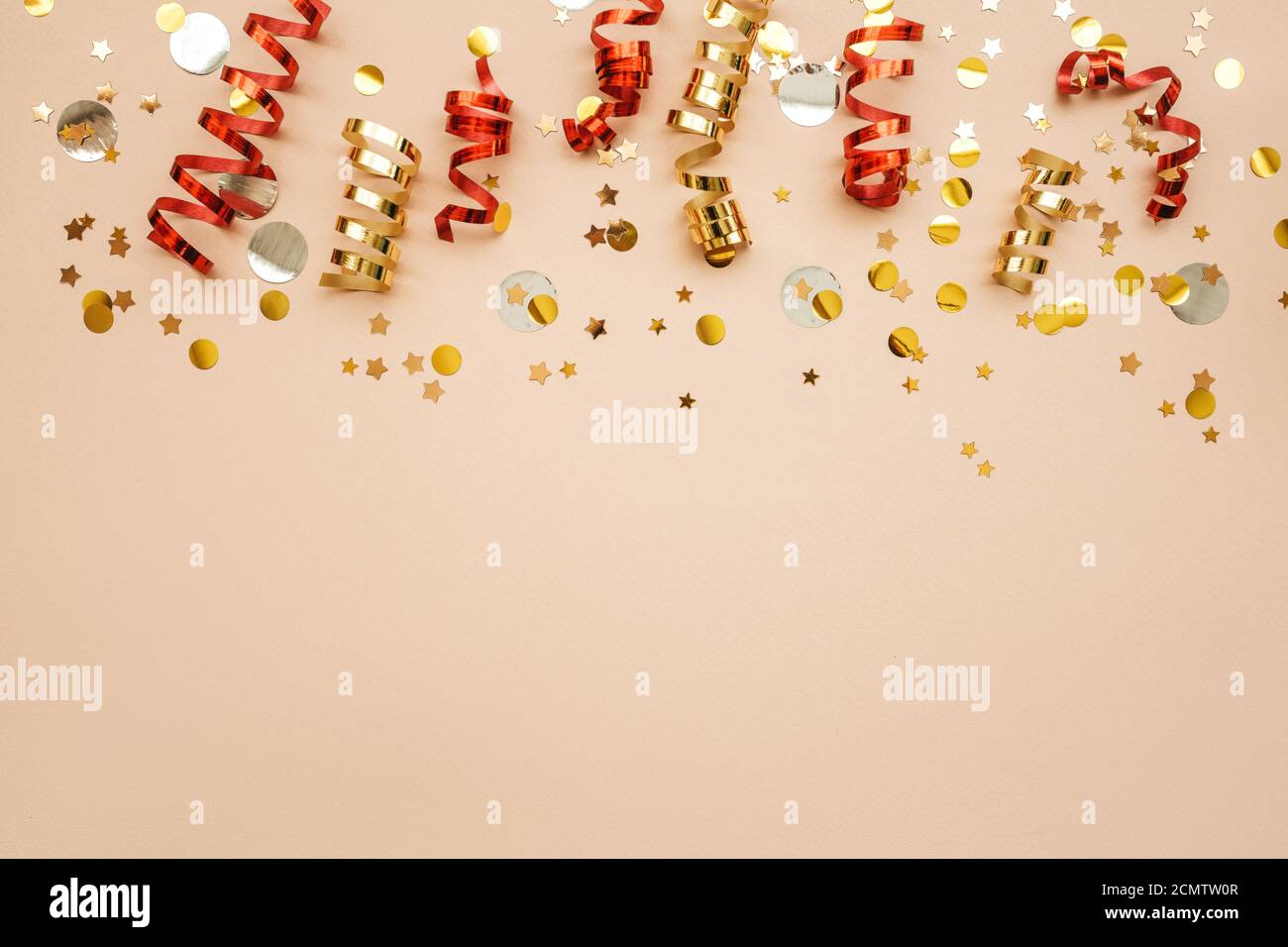 Gold and red Christmas ribbons and confetti on a pink background. Christmas or New Year conceptual background. There is empty space for text at the bottom. Stock Photo