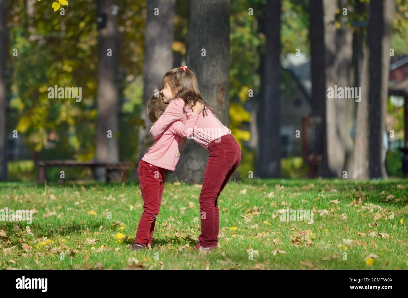 Two little sisters in identical clothes hug each other during a walk in the park on a warm autumn day. The concept of a happy carefree childhood. Stock Photo