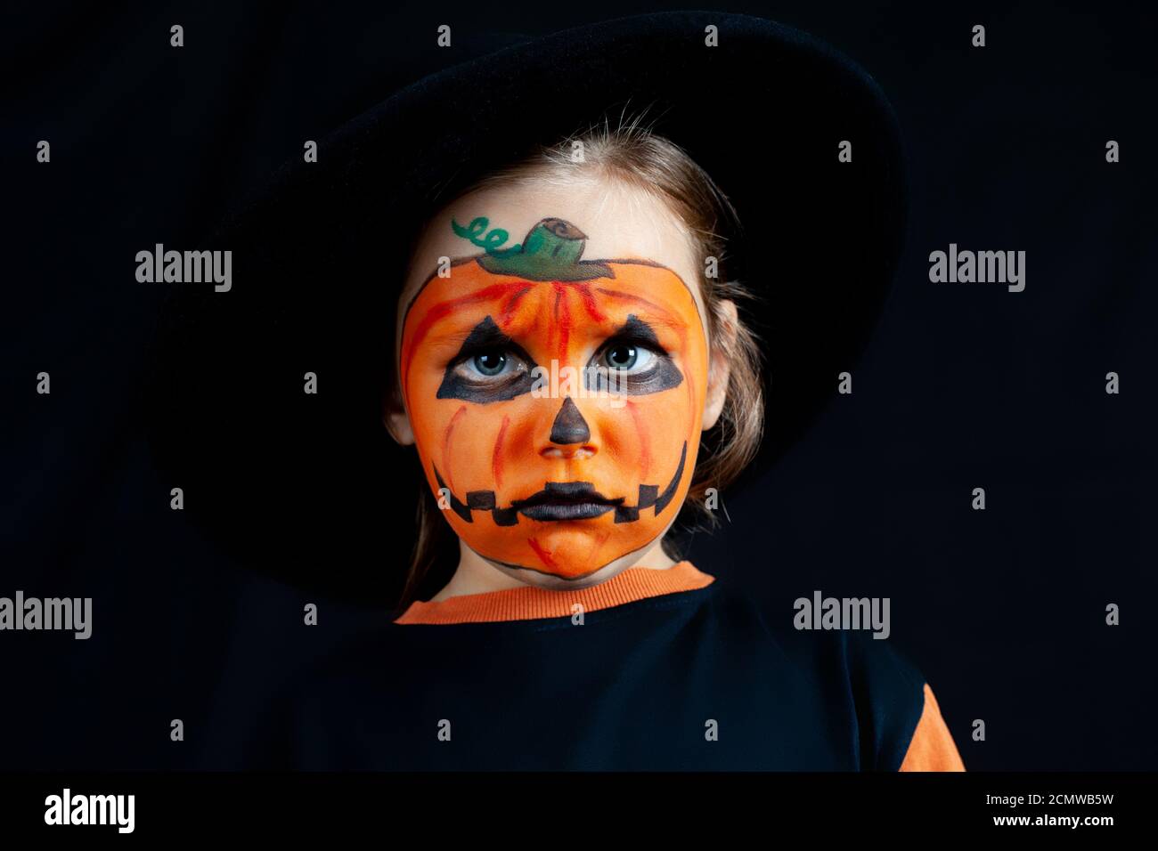 sad girl with pumpkin makeup on her face for Halloween, in a black hat, loneliness and sadness on holiday Stock Photo