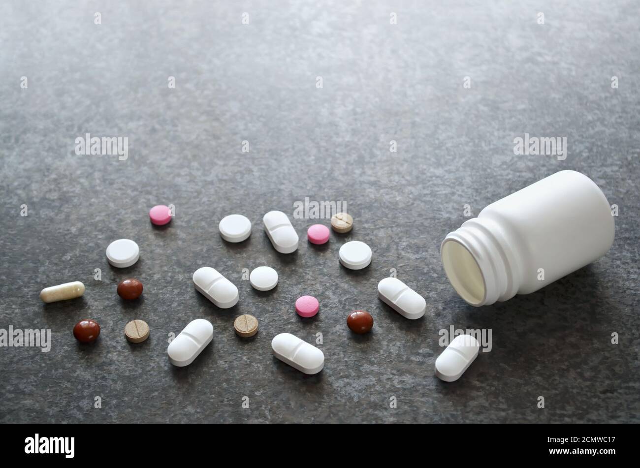 Colorful pills near to an empty white bottle on a dark gray table surface as a background with copy space, selective focus. Stock Photo