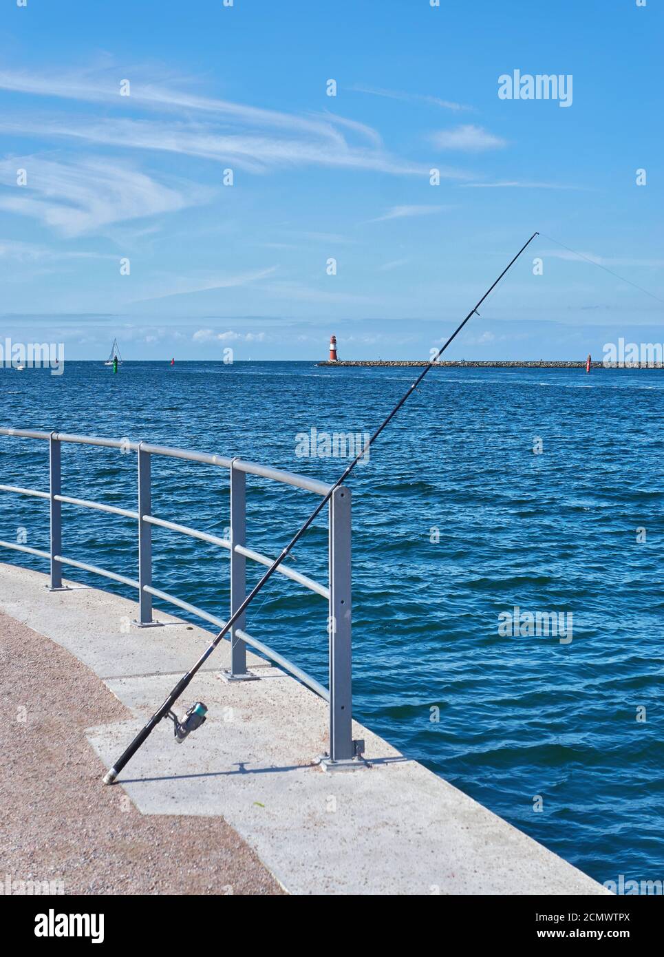 Fishing rod on the Baltic Sea in Warnemünde with the lighthouse on the pier in the background. Stock Photo
