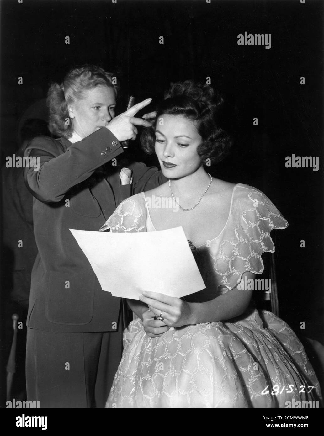 A hairdresser adjusts GENE TIERNEY 's hair while she looks over a diagram of the action for her next scene in THE RAZOR'S EDGE 1946 director EDMUND GOULDING novel W. Somerset Maugham screenplay Lamar Trotti  music Alfred Newman producer Darryl F. Zanuck Twentieth Century Fox Stock Photo