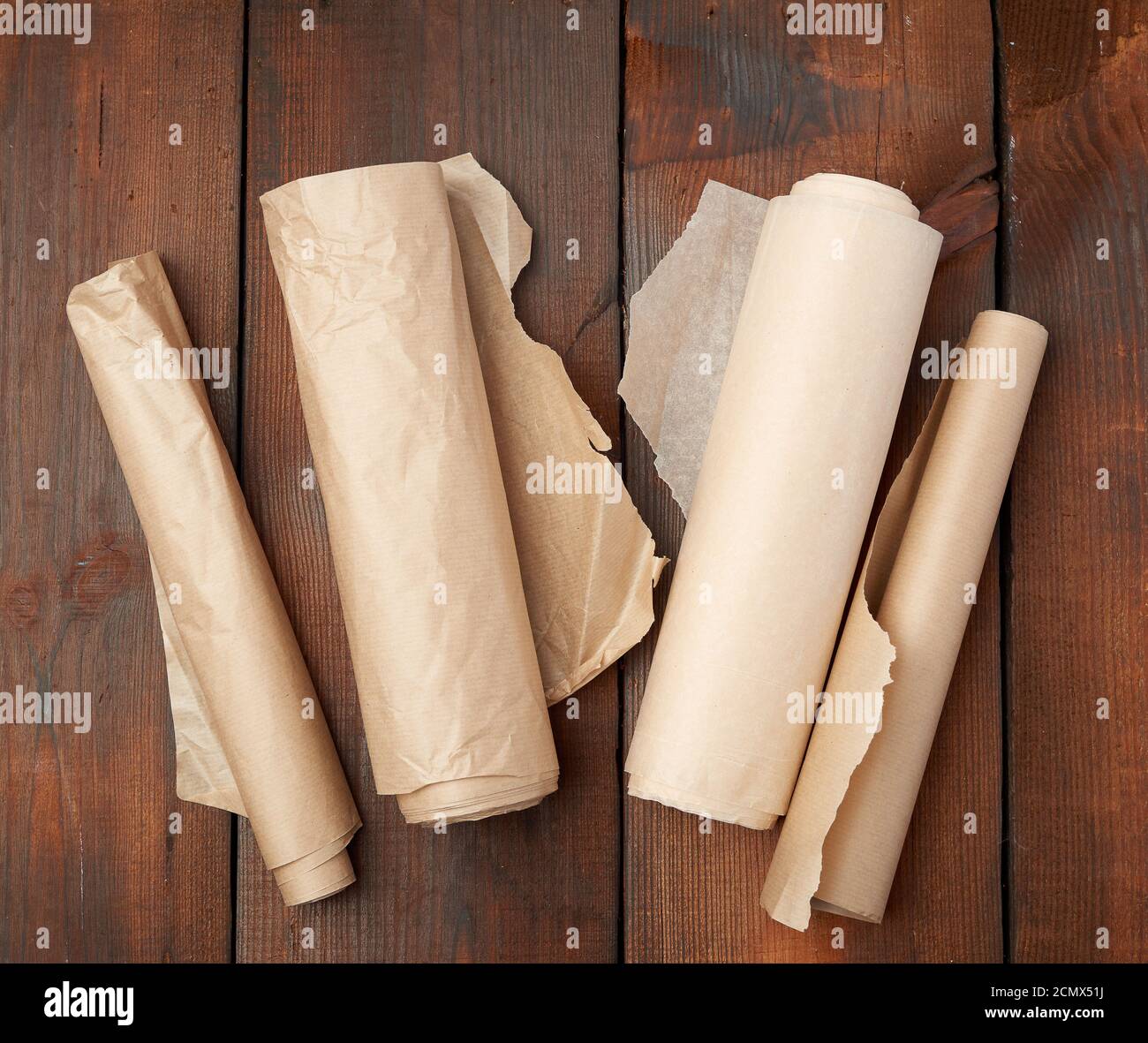 four rolled rolls of brown parchment paper on a wooden background Stock Photo