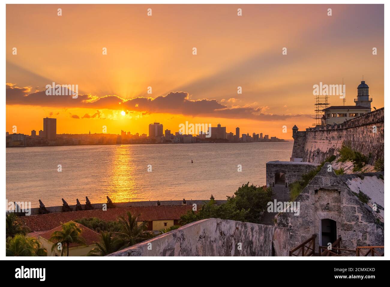 Beautiful sunset in Havana with a view of the city skyline , the El Morro lighthouse and the sun setting over the buildings - Seen from across the bay Stock Photo