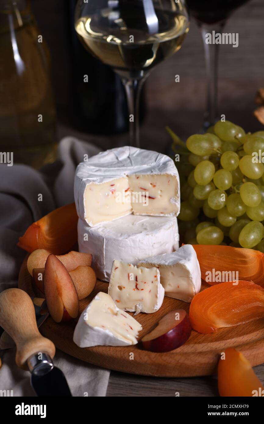 Cheese camembert with white grapes, sliced persimmons and plums, a great appetizer for wine. Stock Photo