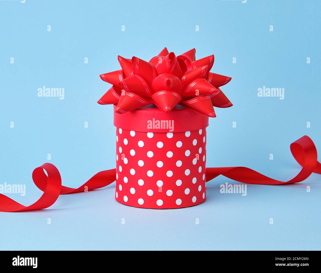 round red cardboard box in white polka dots on top of a bow on a blue background Stock Photo