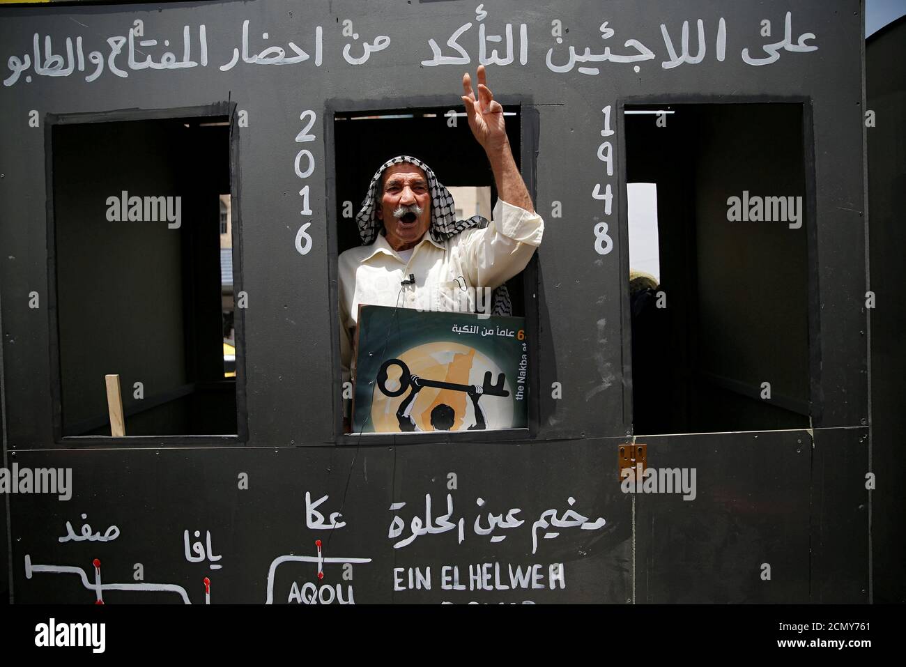A Palestinian man gestures as he rides in a mock train at a scene symbolising the return to homes that Palestinians lost during the 1948 war, on the 68th anniversary of Nakba, in the West Bank town of Bethlehem May 15, 2016. The Arabic writing (top) reads, 'all refugees should make sure to bring the key and the land registry.' REUTERS/Ammar Awad Stock Photo