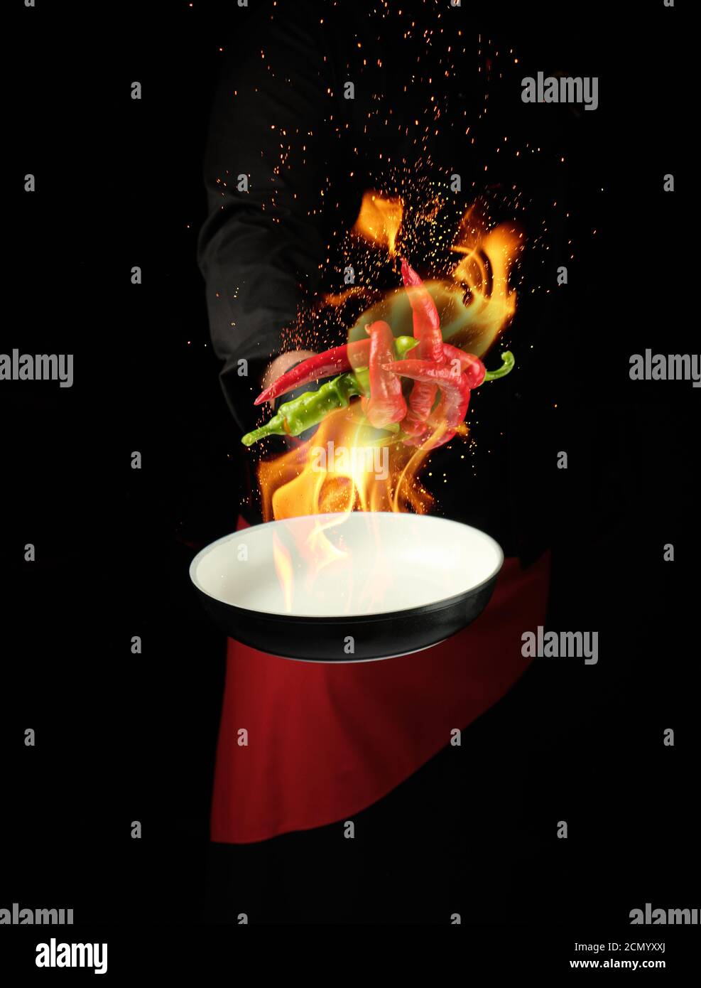 chef in a black uniform holds a round pan and throws up red and green
