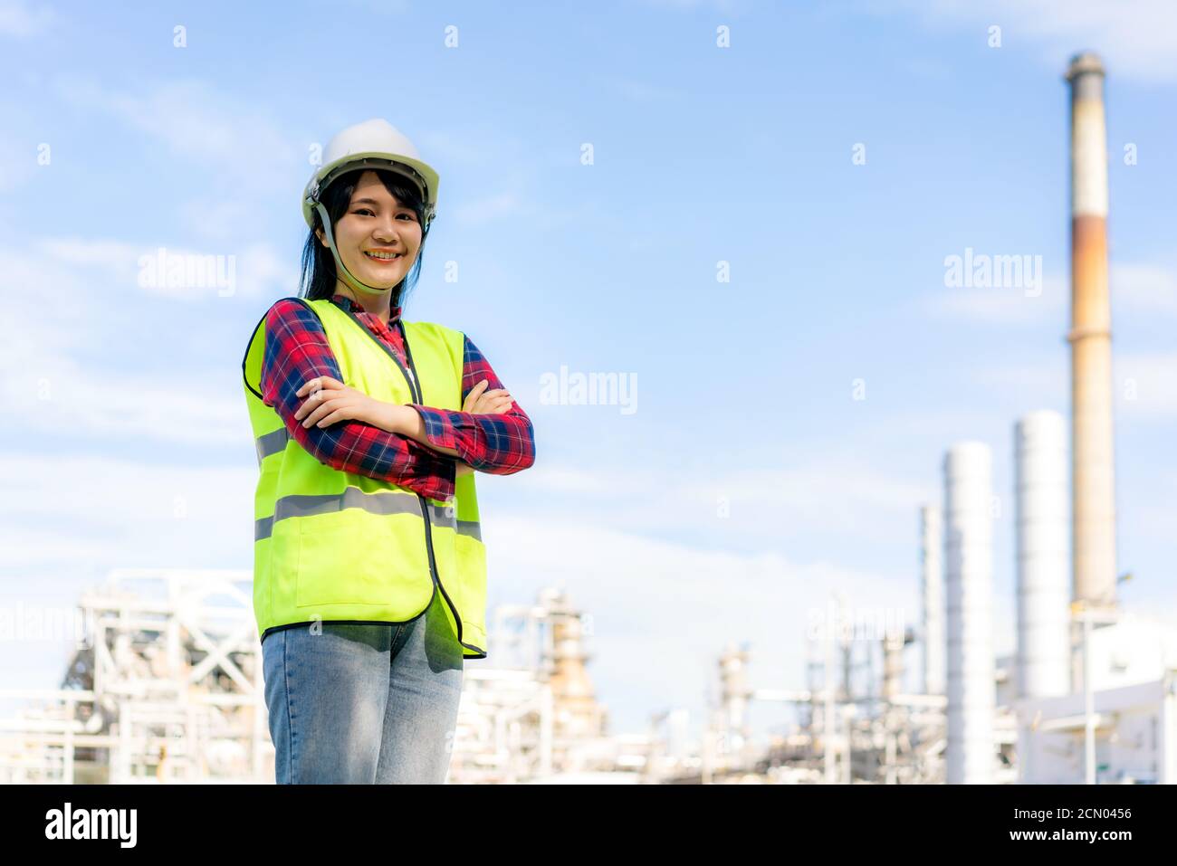 Asian woman engineer arm crossed and smile with confident looking forward to future with oil refinery plant factory in background. Stock Photo