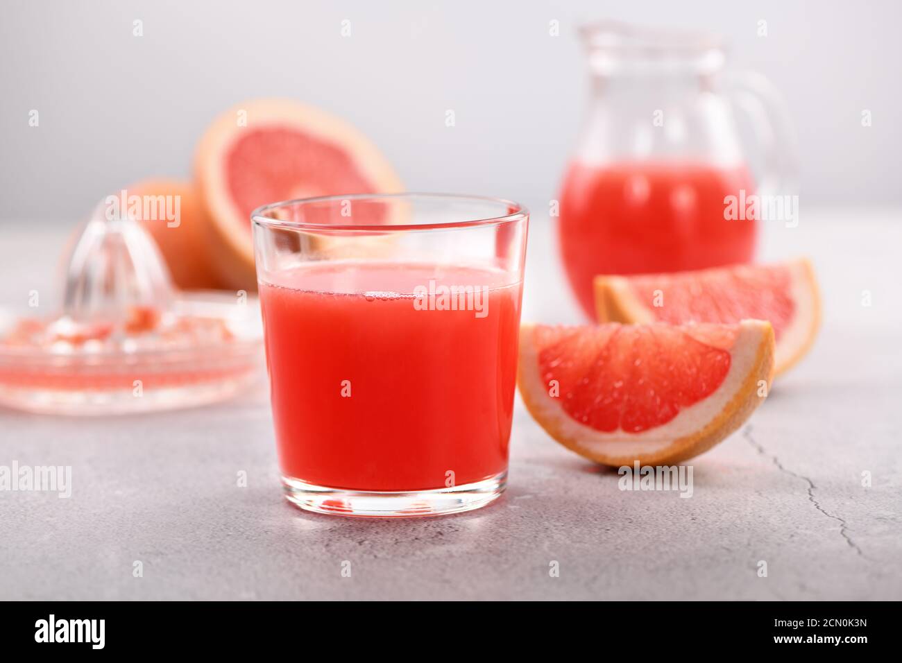 A glass of freshly made grapefruit juice and slices of fresh fruit on a light concrete background. H Stock Photo
