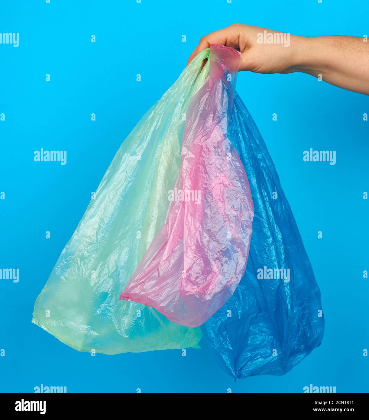 hand holds empty multi-colored plastic bags on a blue background Stock Photo