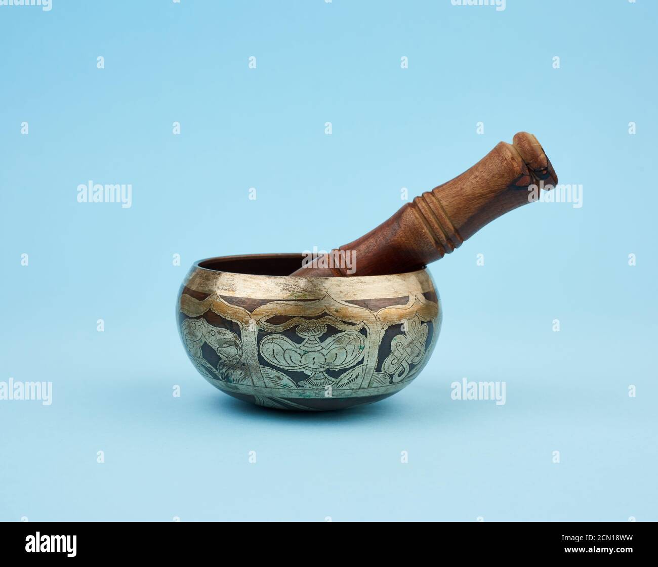copper singing bowl and wooden stick on a blue background, a Tibetan