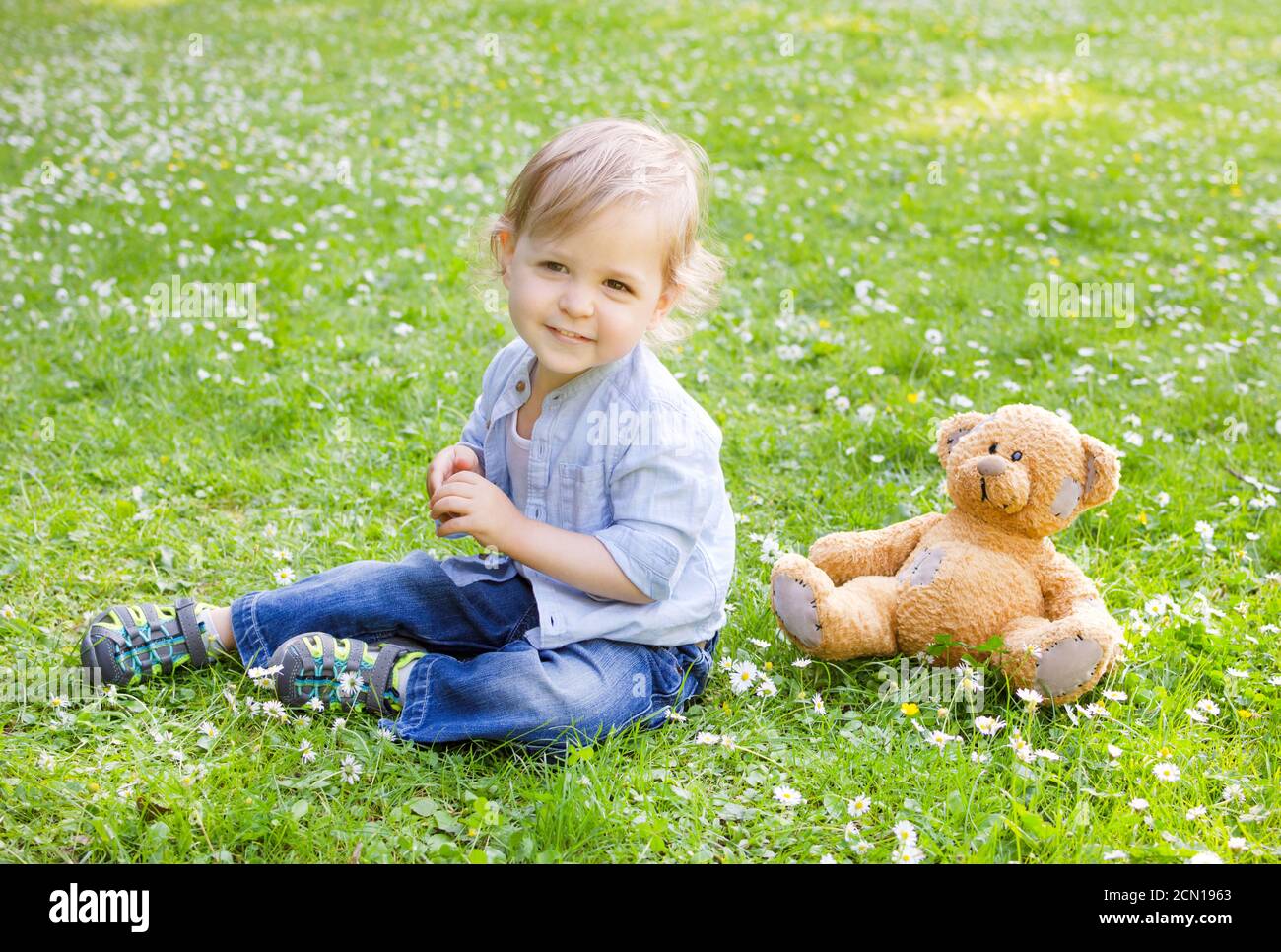 Happy cute little child standing on the grass in the park with his ...