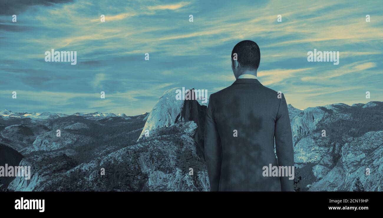 A man in a suit on top of a mountain. Beautiful landscape of mountains. Clouds in the sky Stock Photo