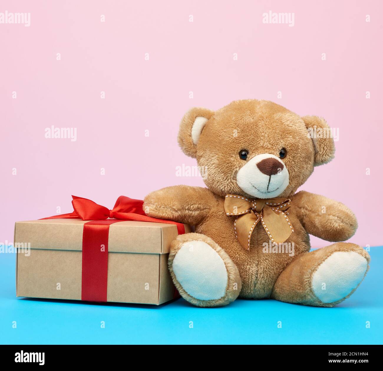 cute little brown teddy bear holds a brown box with a red ribbon Stock ...