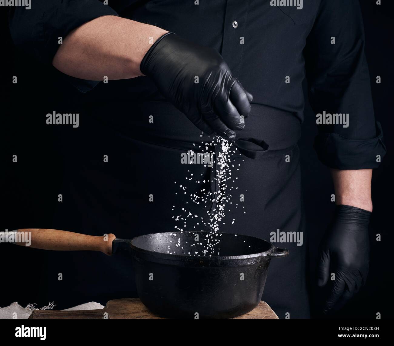 male cook in black uniform and latex gloves salt food in a black cast