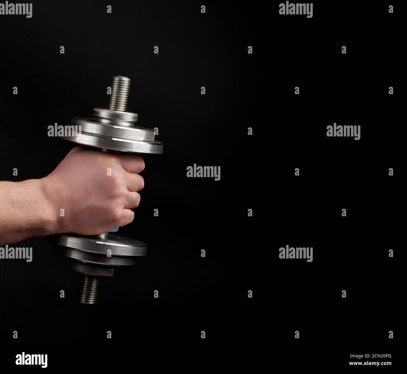 man holds steel dumbbells in his hands, his muscles are tense, low key Stock Photo
