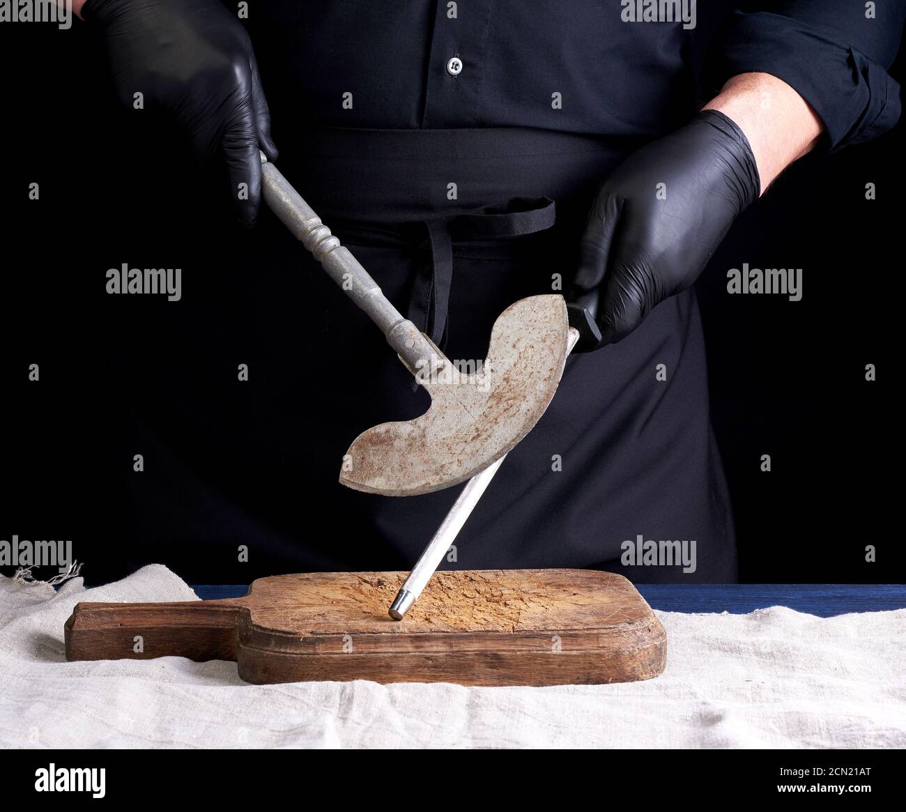 male cook in black uniform and black latex gloves holds a large sharp
