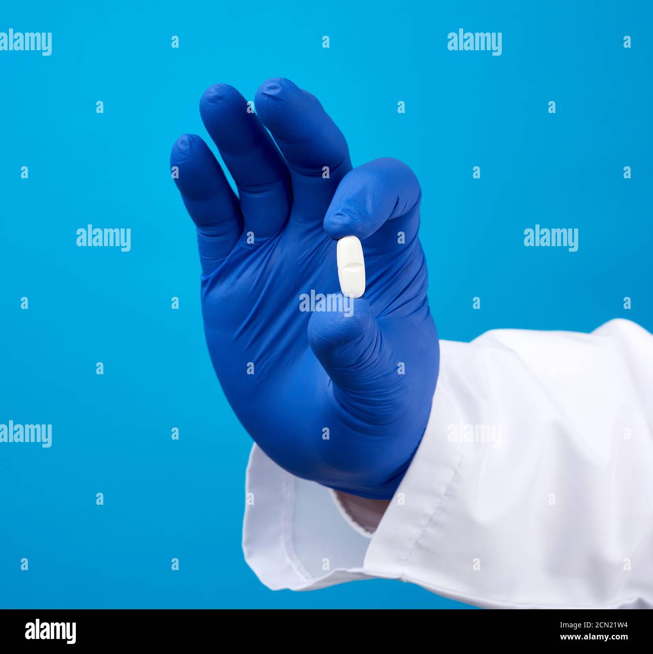 male hand in blue sterile gloves holds an oval white pill, medical