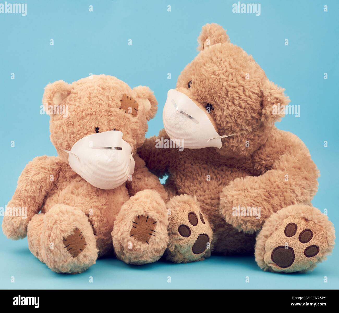 big brown teddy bears are sitting in medical masks on a blue background Stock Photo