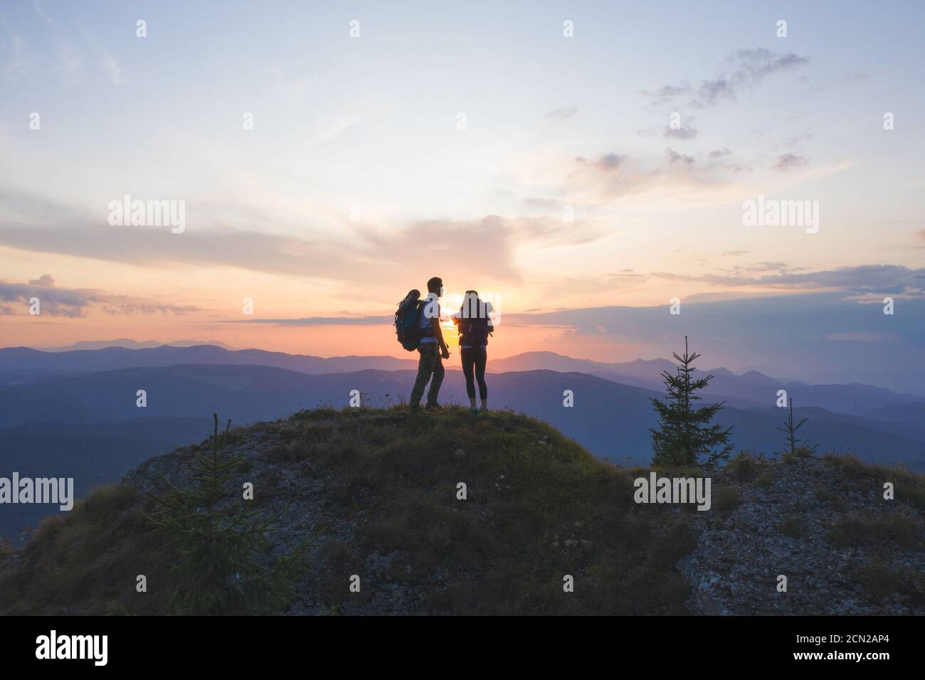 Couple travelers Man and Woman sitting on cliff watching the sunset ...