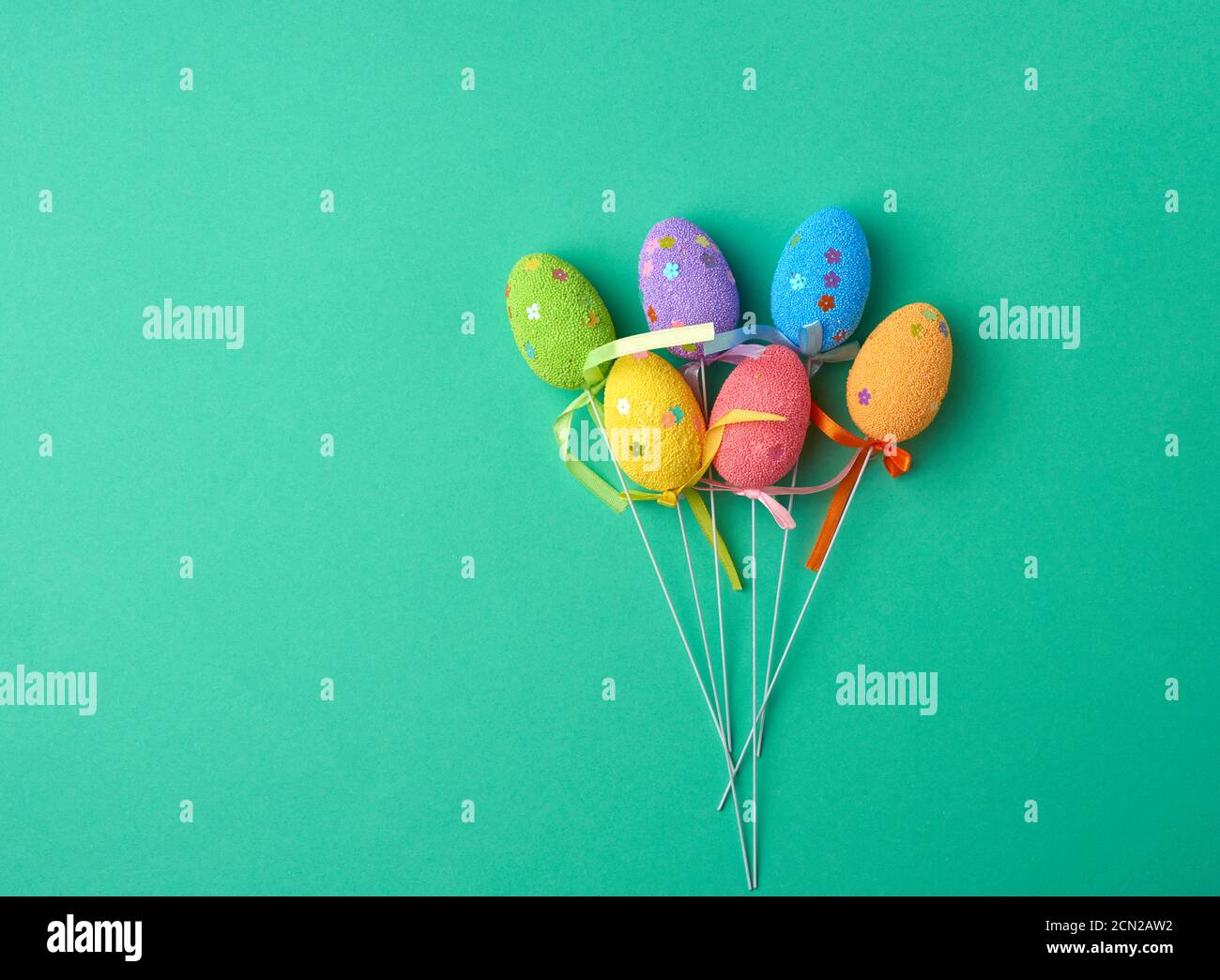 multi-colored decorative Easter eggs on sticks on a green background, festive backdrop, top view Stock Photo