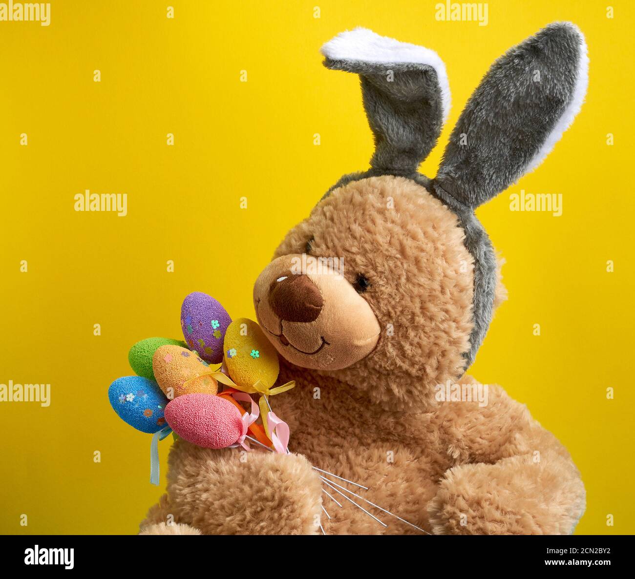 big cute brown teddy bear holding colorful Easter eggs, wearing a