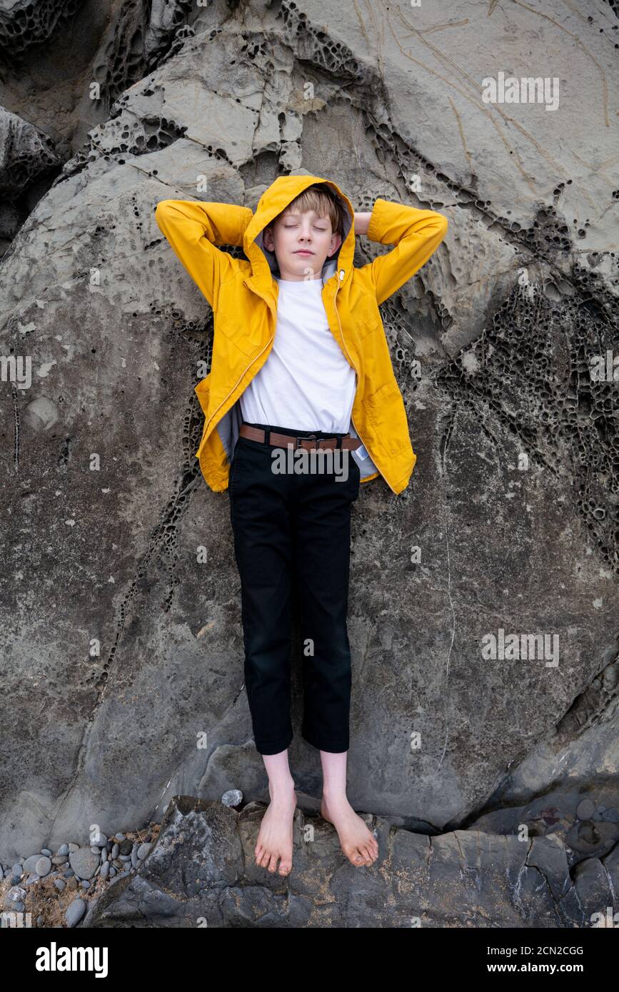 Full body portrait of tween lying on coastal stones with eyes closed ...