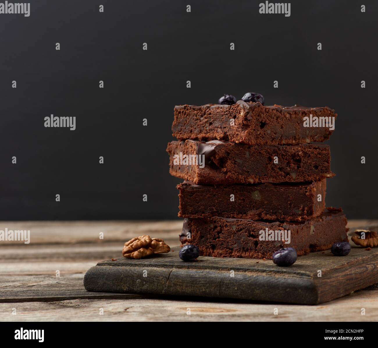 stack of square baked slices of brownie chocolate cake with walnuts on a wooden surface. Cooked home Stock Photo