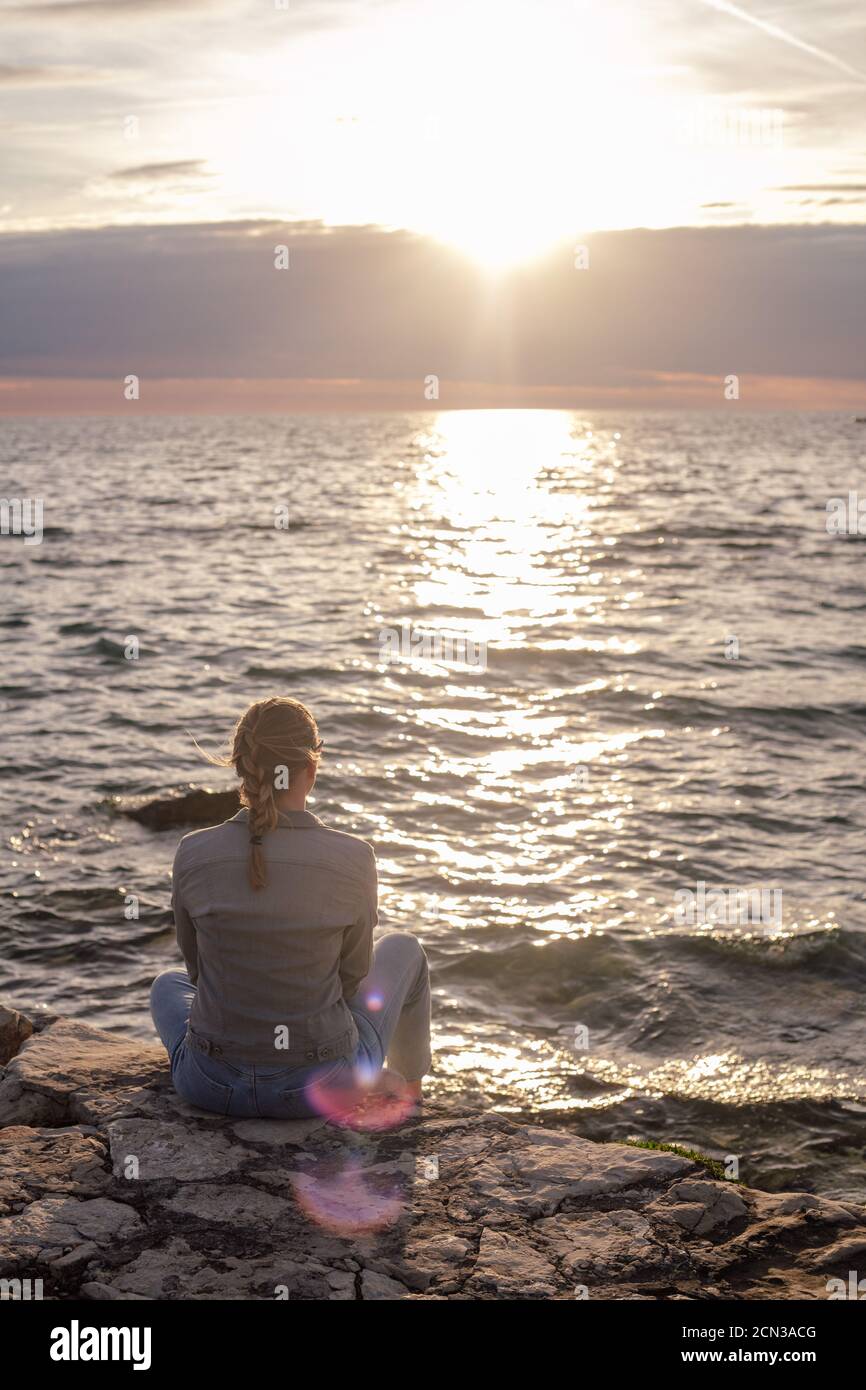 Back view of woman sitting by the sea Stock Photo - Alamy