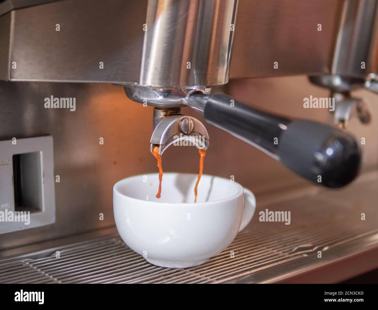 Fresh coffee pouring down from the portafilter of espresso machine into the white ceramic cup. Making hot coffee with the espresso machine. Stock Photo