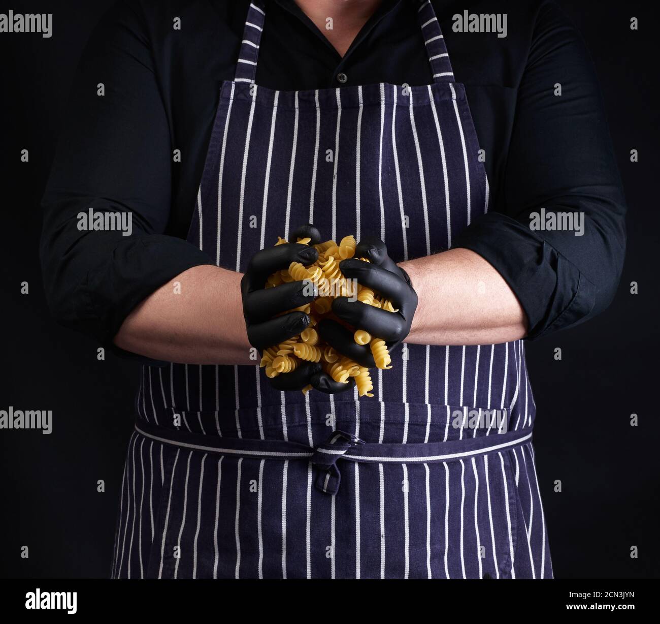 male cook in a striped apron and black latex gloves hold raw fusili