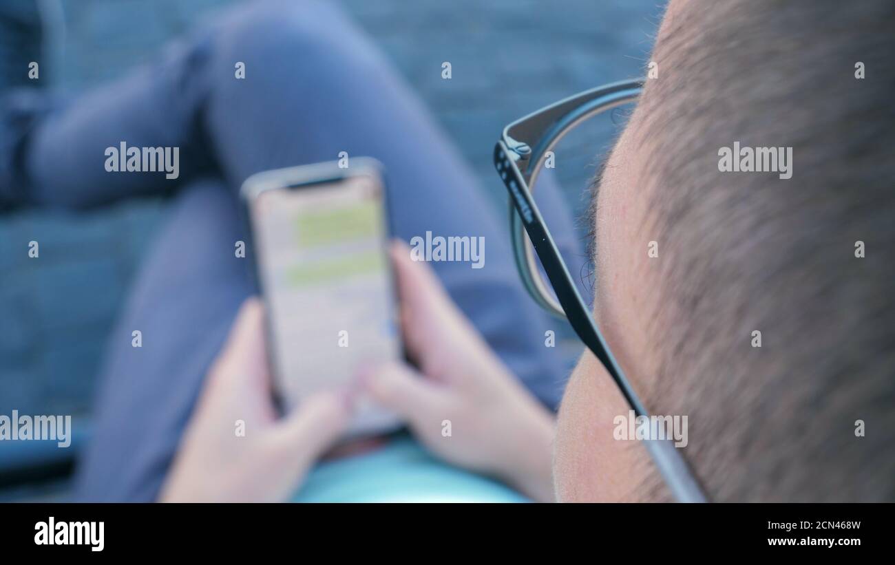 Man using his smartphone writing a message sitting on a bench. Stock Photo