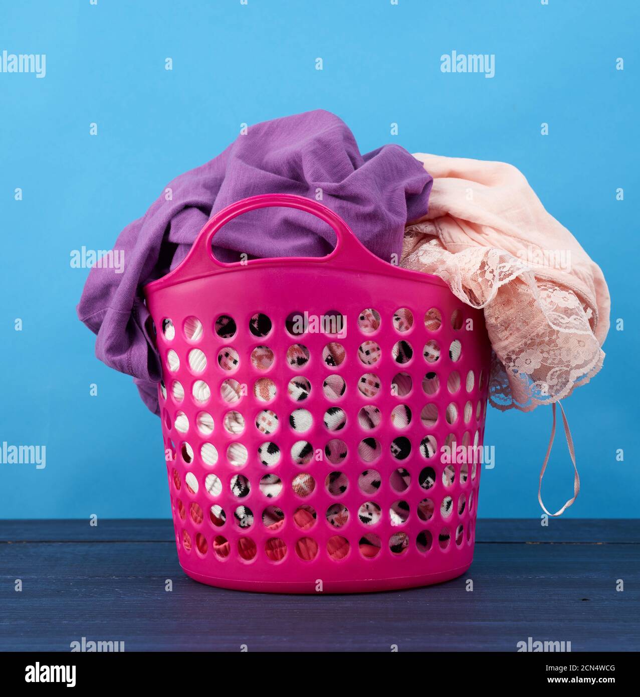 pink plastic basket full of clothes and linen on a blue background Stock Photo