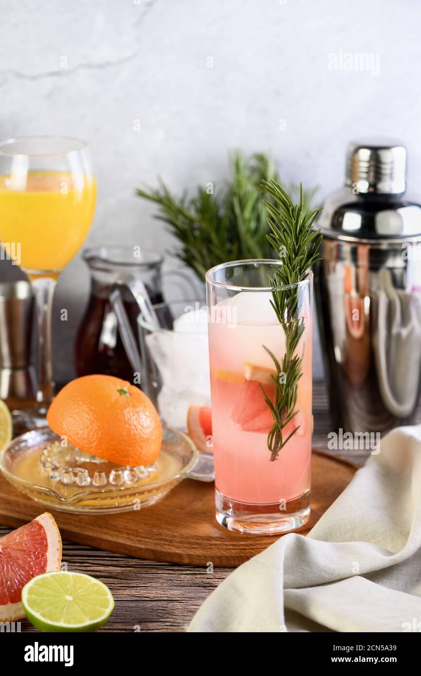 Gin cocktail with rosemary and pomegranate on a table among citrus
